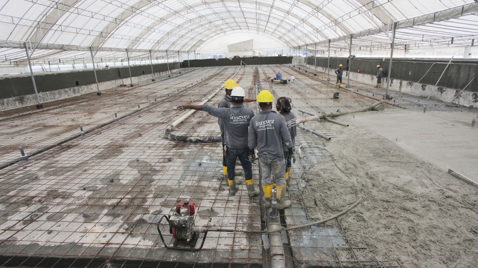 Construction workers from Innovez Engineering are dressed in safety gear, and survey a wide section of the pool floor. A temporary tentage shelters the work area. Concrete casting works appear to be underway at the Singapore Island Country Club.