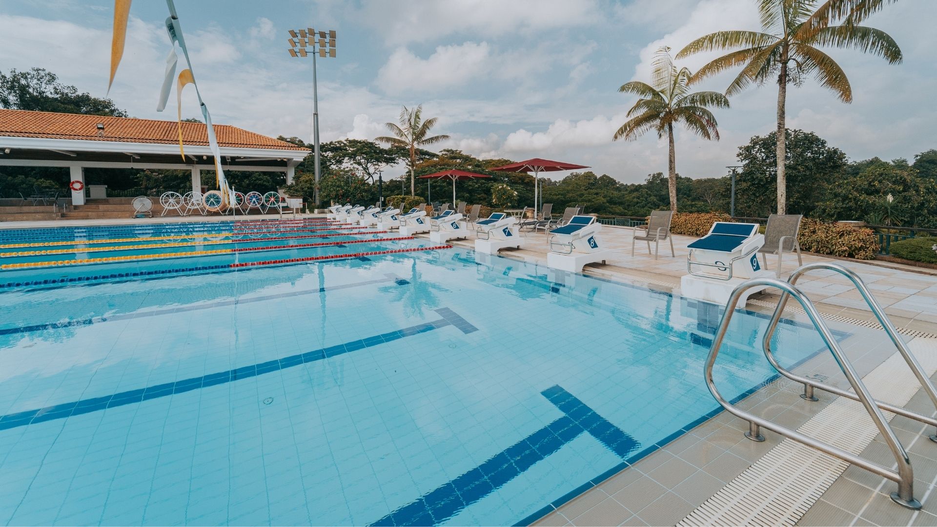 Close-up of the upgraded competition pool at the Singapore Island Country Club. Starting blocks line up at one end, and half of the pool is divided with lane ropes. Grab rails have been built atop the pool gutter at the edge, and pool pennants hang above.