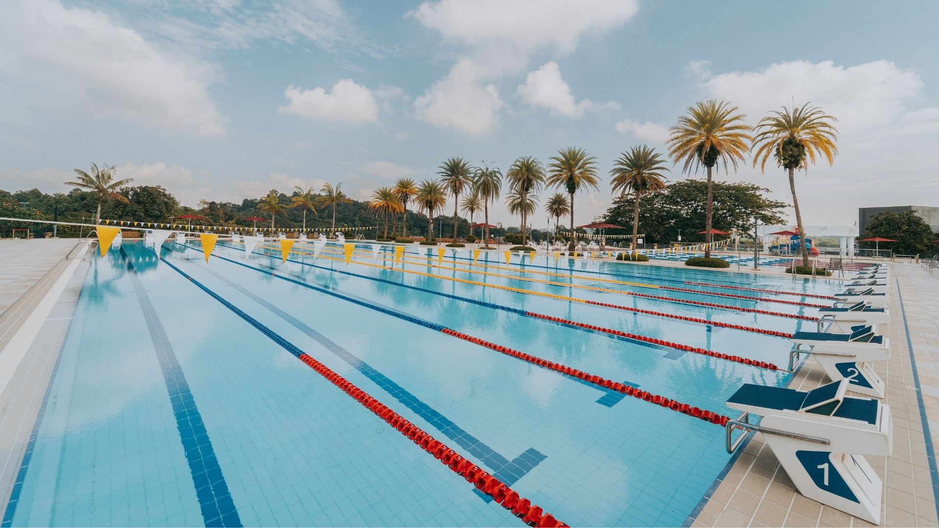 Diagonal view of the 50-metre competition swimming pool at the Singapore Island Country Club, which looks like it has been refurbished. The pool tiles and ropes are clean, the starting blocks look solid, and the pool flags hanging across are taut.