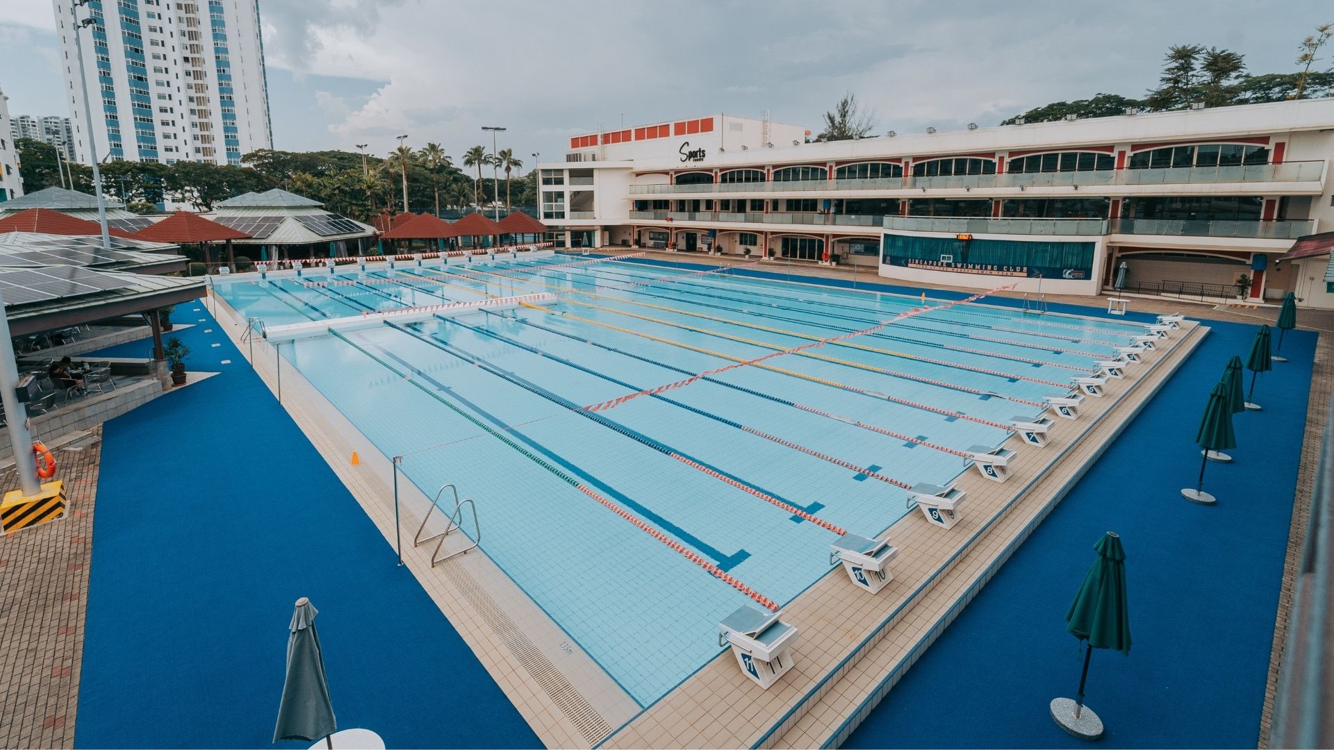 Diagonal view of the 12-lane competition pool at the Singapore Swimming Club. Starting blocks line each end, and grab rails can be found spaced out along the length of the pool.