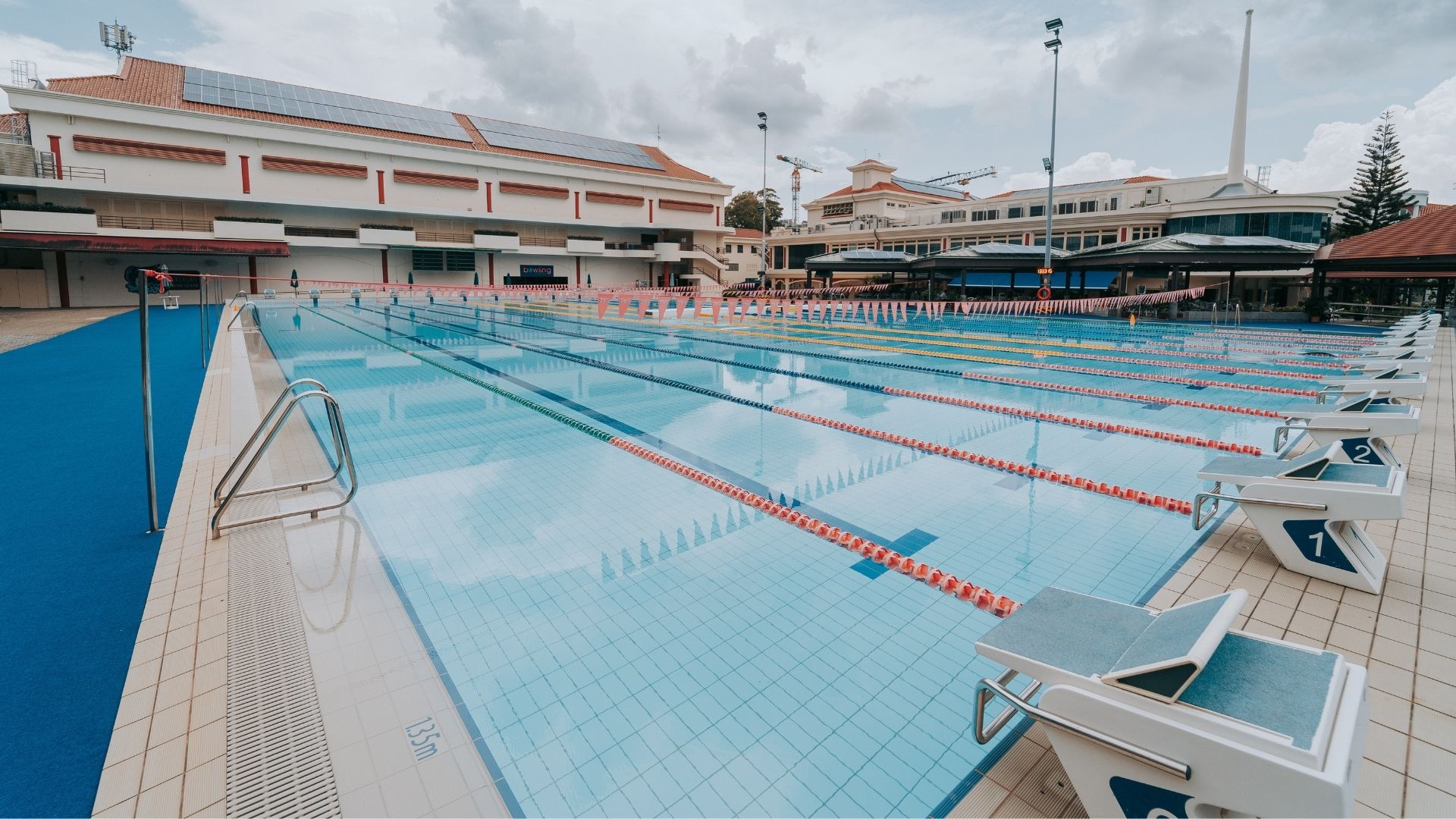 Diagonal view of the Singapore Swimming Club after renovation works. The Olympic-sized competition pool looks well-equipped with various pool accessories such as flags, ropes, starting blocks, and grab rails.