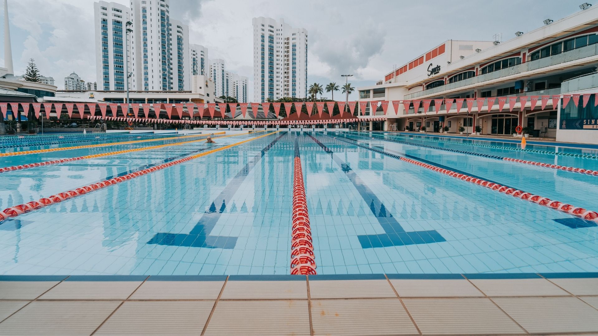 Eye-level view of the Olympic-sized competition pool at the Singapore Swimming Club, replete with pool accessories that include rows of flags above the water, and sturdy pool lane ropes.