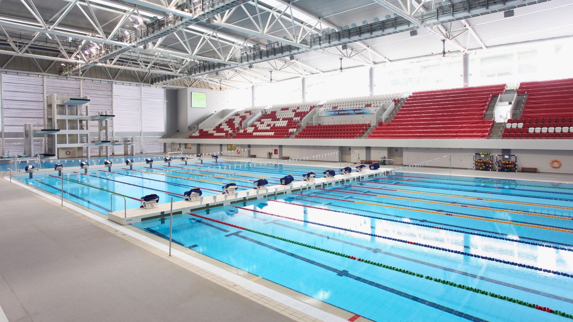 The OCBC Aquatic Centre at Singapore Sports Hub (now known as The Kallang). A bulkhead separates the indoor training and competition pools. The competition pool is equipped with starting blocks and diving boards. Spectator stands line the pool length.