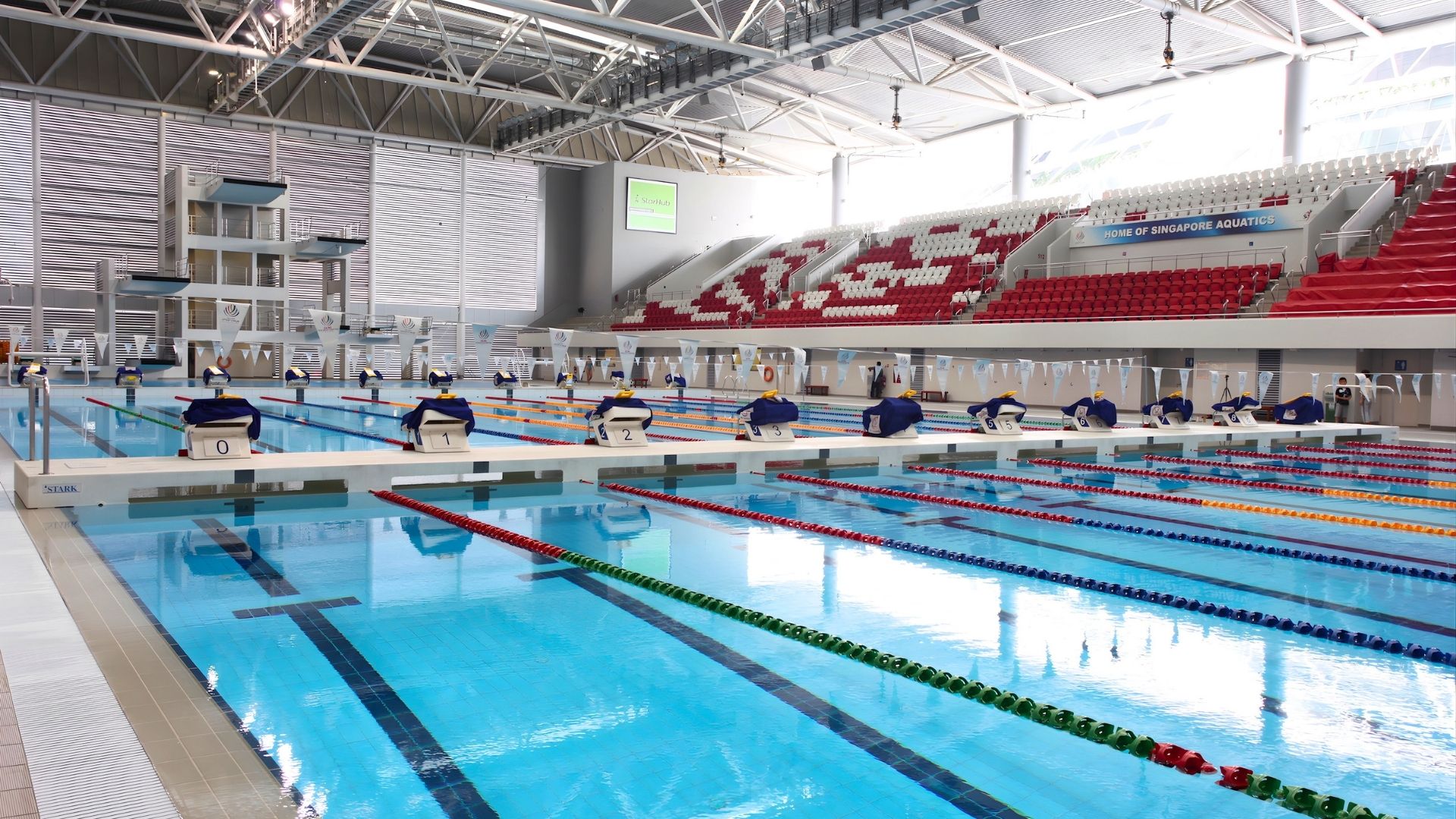 Eye-level view of the swimming pools at the OCBC Aquatic Centre, located at the Singapore Sports Hub/The Kallang. They have been compartmentalised into a training pool and competition pool via a white bulkhead. Starting blocks face towards the competition 