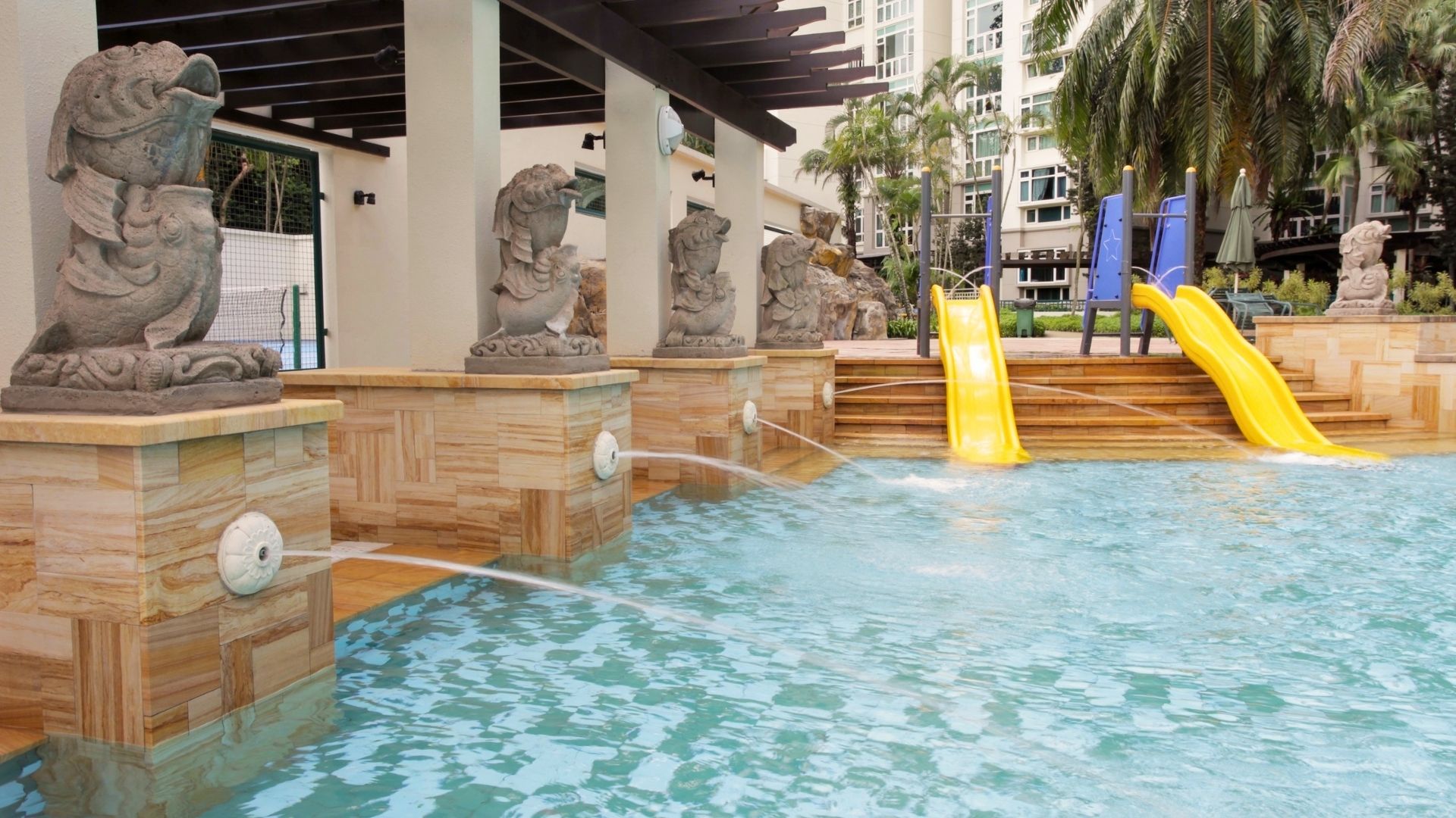 Bright yellow water slides lead into the children's wading pool at Summerhill condominium in Singapore. Merlion-looking statues adorn one end, with water jets spraying water into the pool below them.