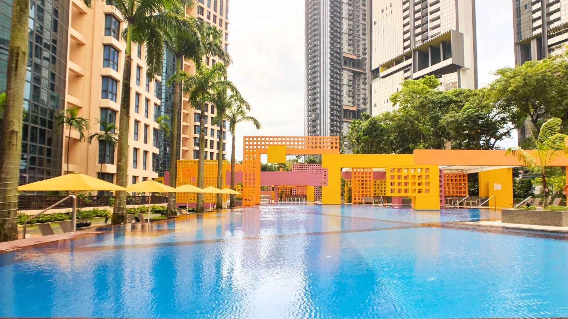 Eye-level view of the swimming pool at Tanglin View Condominium, with its recognisable geometric architectural design in yellow and orange. Shaded lounge chairs are neatly-spaced out on the pool deck.