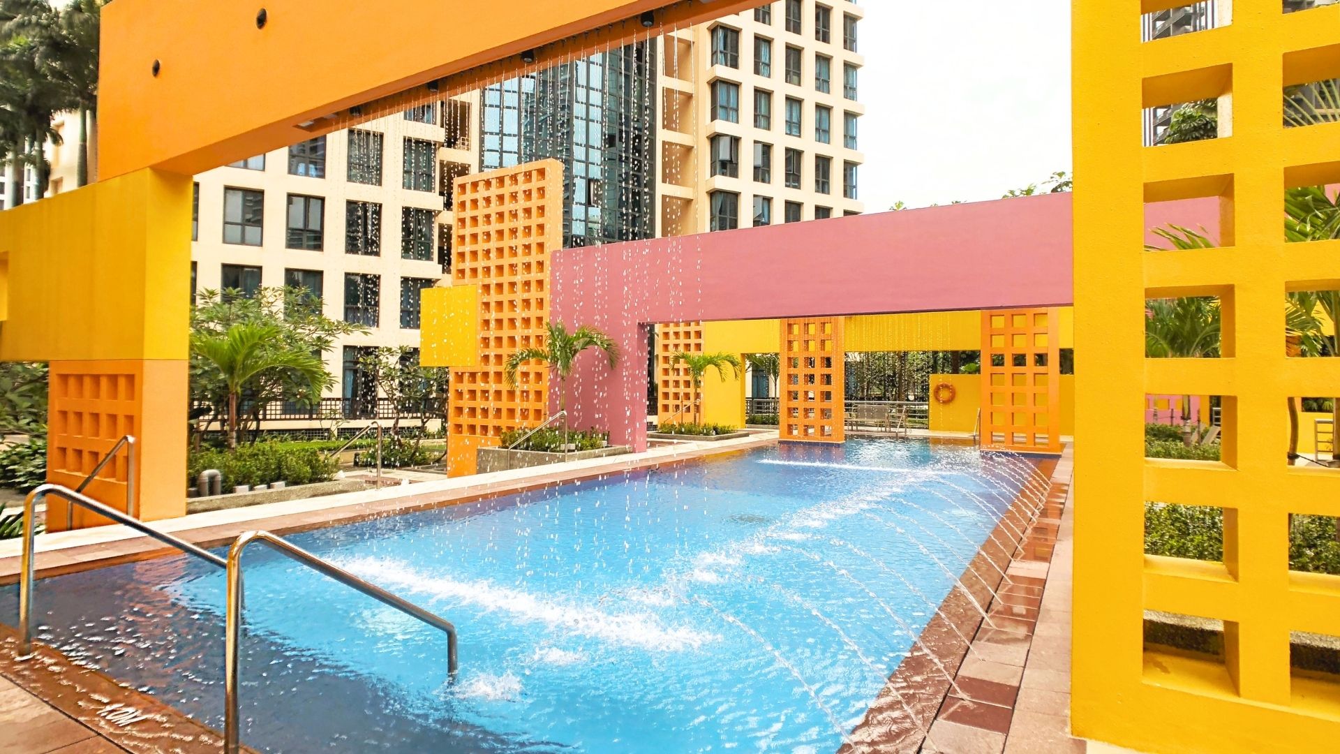 Close-up of the water features and grab rails leading into the pool at Tanglin View Condominium, Singapore. Water fountains shoot streams of water in an arc to one side, whilst thin streams of water fall from the orange structure above the pool gracefully.