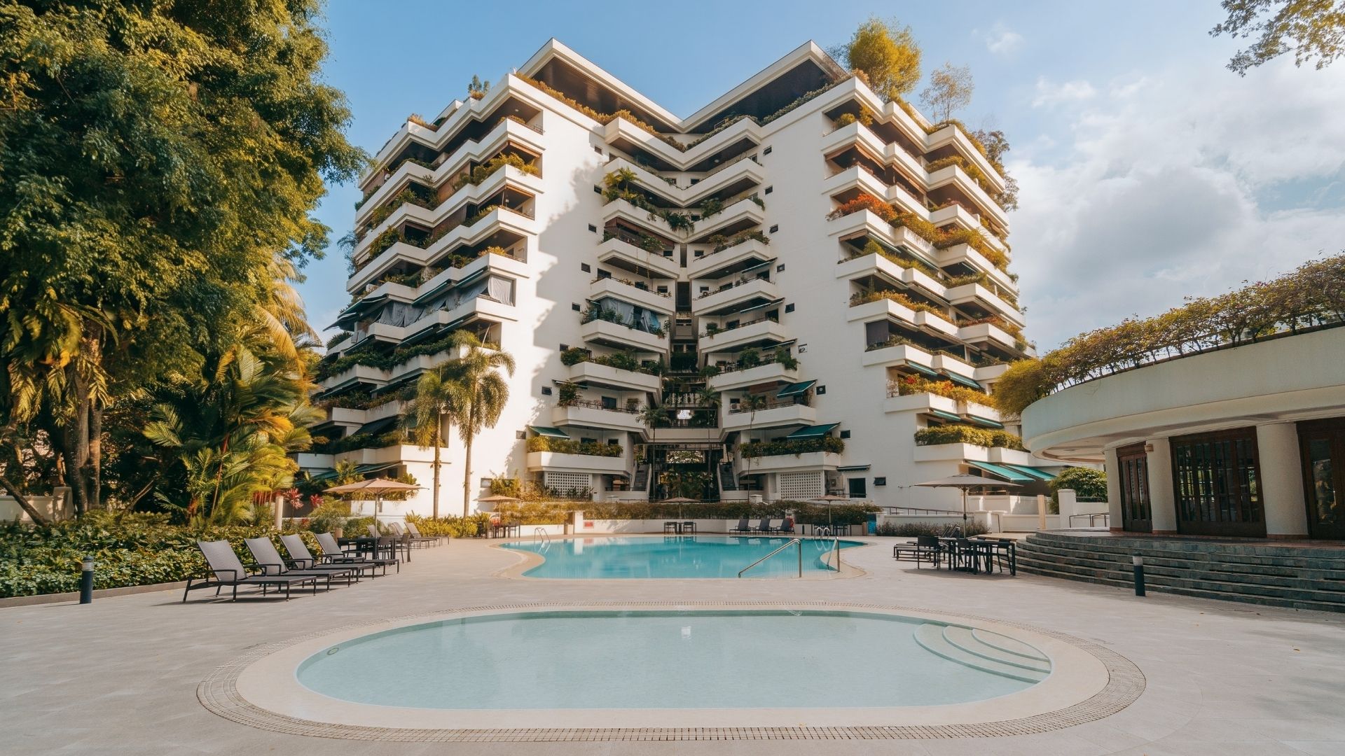 Full view of The Arcadia Condominium facing upwards from the ground level. The main pool and children's wading pool are aligned in front of the apartment blocks. Both pools are tastefully designed in circular shapes, and surrounded by a spacious pool deck.