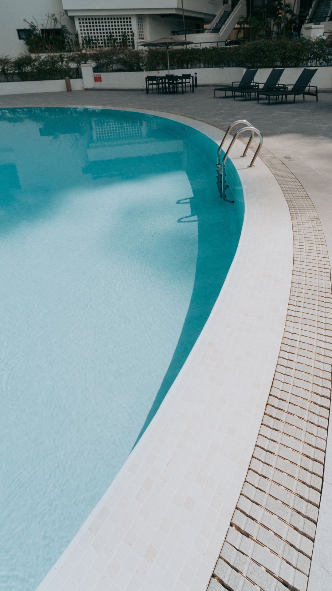 Close-up portrait view of the swimming pool, tiles, and gutter at The Arcadia condominium in Singapore. Spanish porcelain tiles in neutral tones cover the pool deck, with matching procelain tile gratings for a seamless look.