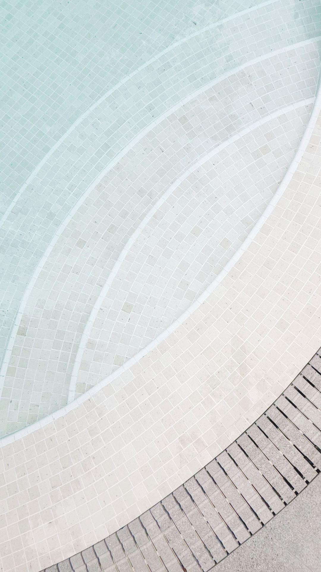 Close-up of the upgraded swimming pool steps at The Arcadia, which lead downwards in widening arcs. The pool is made up of elegant cream-coloured Spanish glass mosaic finishes, with a light grey Spanish porcelain-tiled deck, and matching gratings.