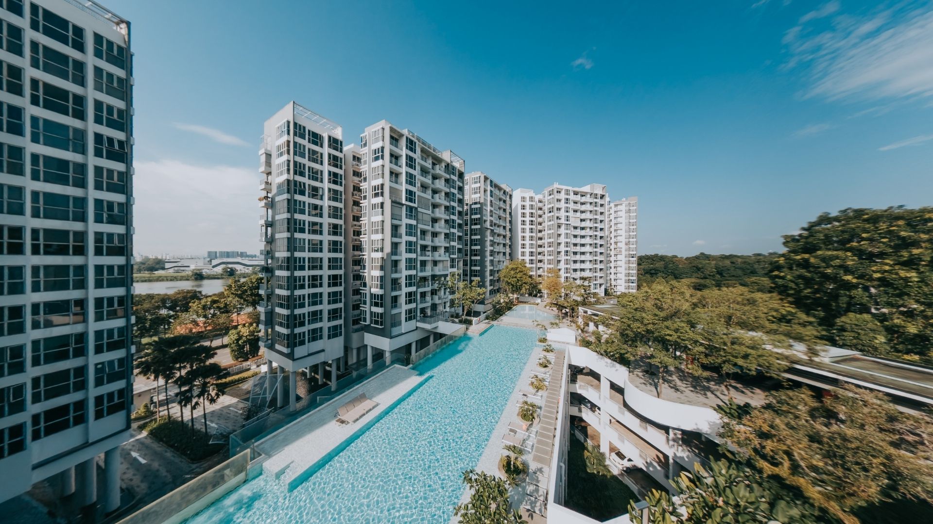 Bird's-eye view of The Estuary, a waterfront condominium with swimming facilities overlooking Lower Seletar Reservoir. The long swimming pool spans several residential blocks, and is surrounded by verdant landscape with a resort-style feel.