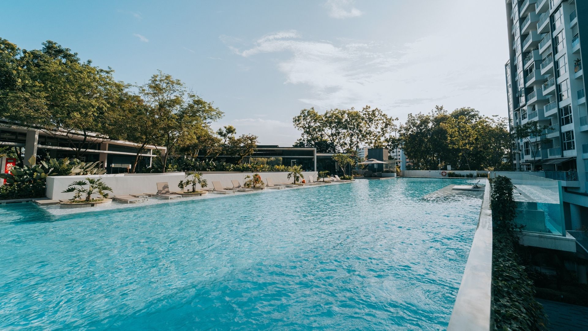 The main swimming pool at The Estuary Condominium in Singapore. Lounge chairs on the pool deck are tastefully spaced apart, with potted plants between the gaps.