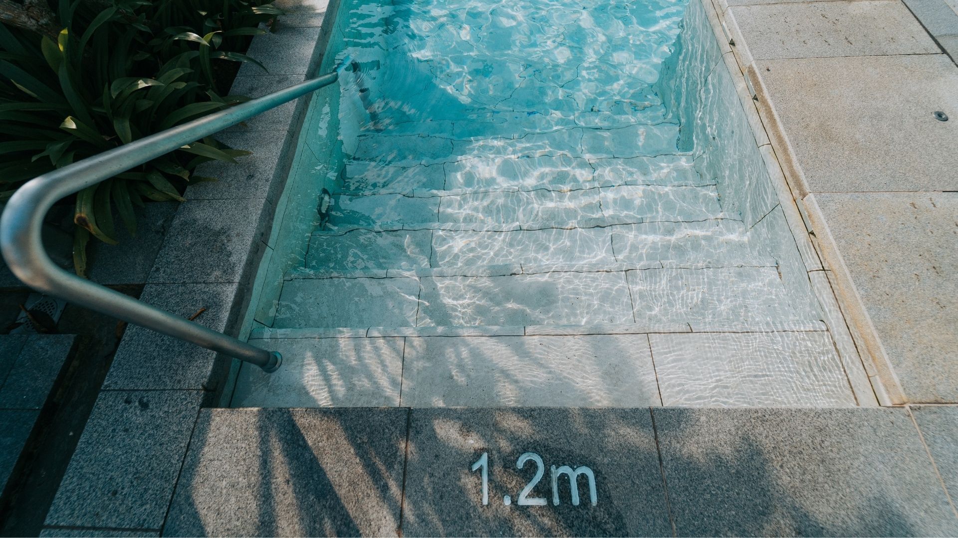The swimming pool steps at The Estuary Condominium in Singapore, with a sturdy grab rail positioned next to it. The pool depth, 1.2 metres, is indicated on the concrete floor tiles before the steps.
