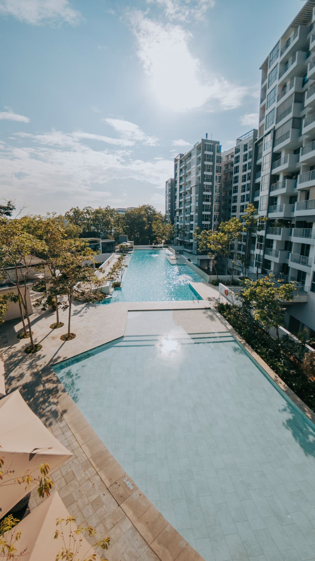 Portrait overhead shot of the swimming pools at The Estuary Condominium, Singapore. They comprise a main 50-metre lap pool, jaccuzi pool areas, and a large children's wading pool.