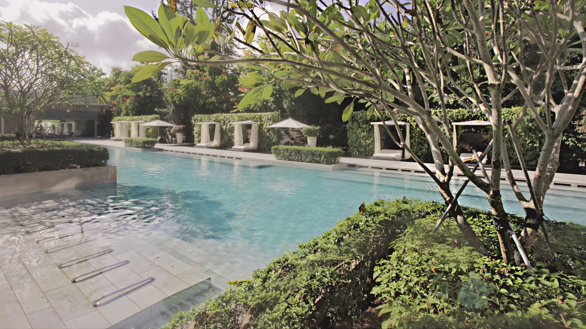 The Glyndebourne Condominium swimming pool, after upgrade works have been completed. Steps leading down into pool are carved in large slabs of concrete and look newly-tiled, with grab rails close to the floor.