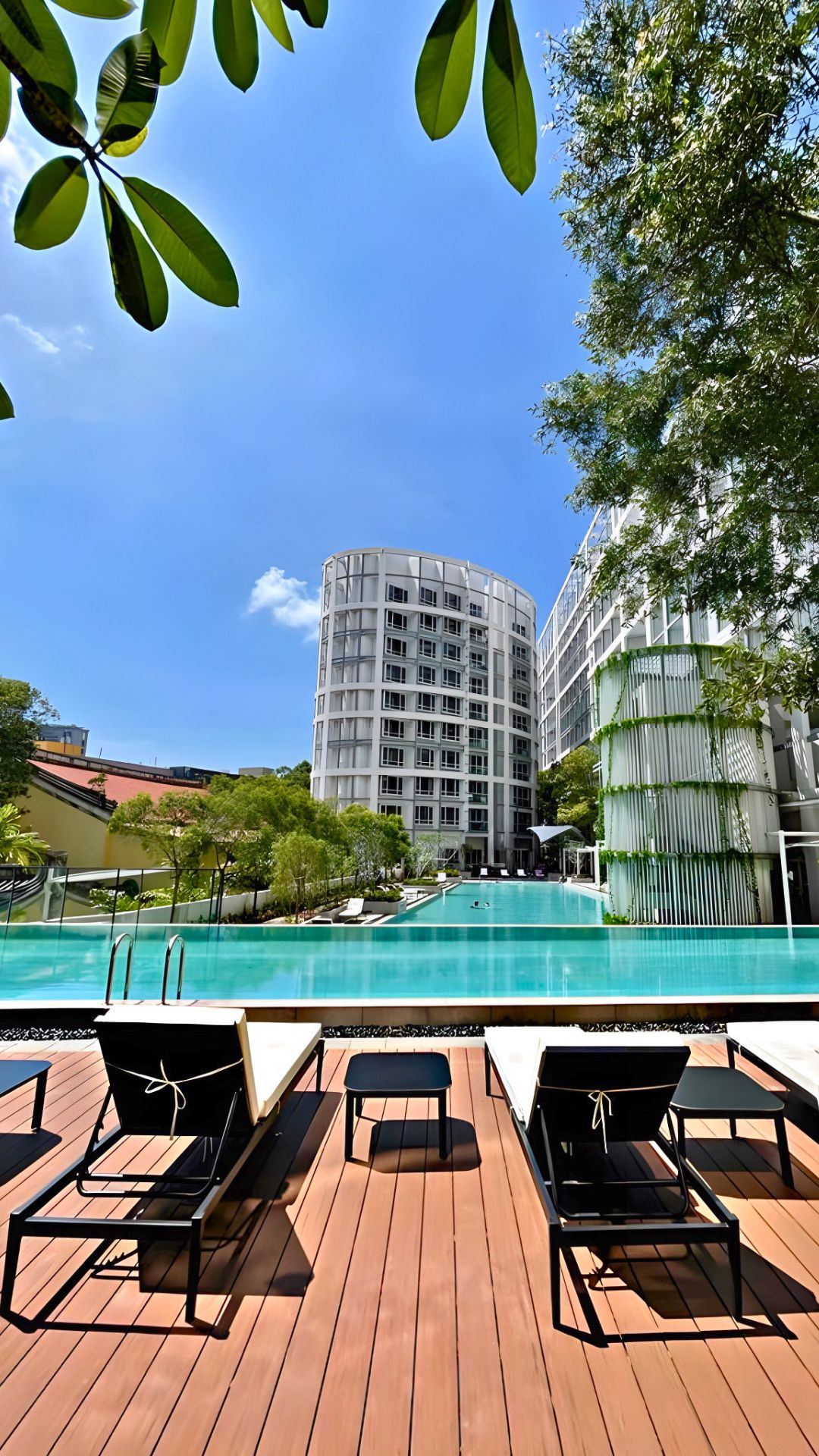 The fully redesigned and renovated pool deck at Visioncrest Residence in Singapore. Adjustable white lounge chairs are paired with short tables, and overlook the condominium's pools and apartments.