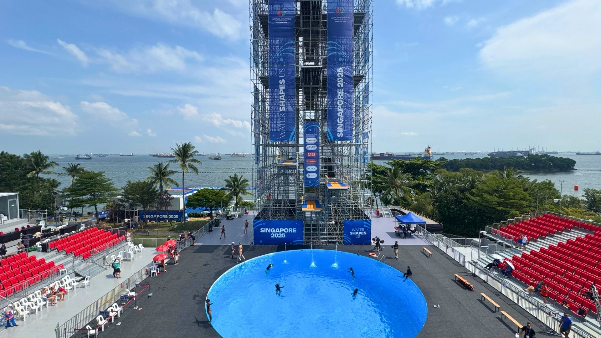 Aerial view of the World Aquatics Championships Singapore, with the six-metre deep high diving pool at Sentosa. Swimmers are swimming in the circular pool at the bottom, and red spectator stands line the sides.