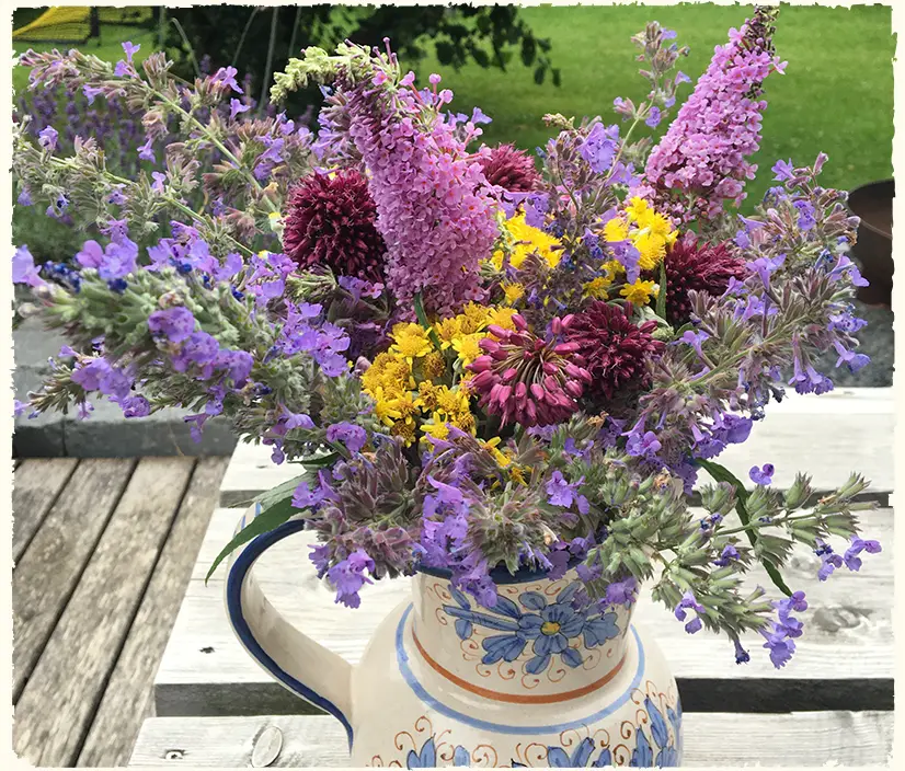 Ein bunter Wildblumenstrauß in einem dekorativen Steingut-Krug steht auf einem Terrassentisch