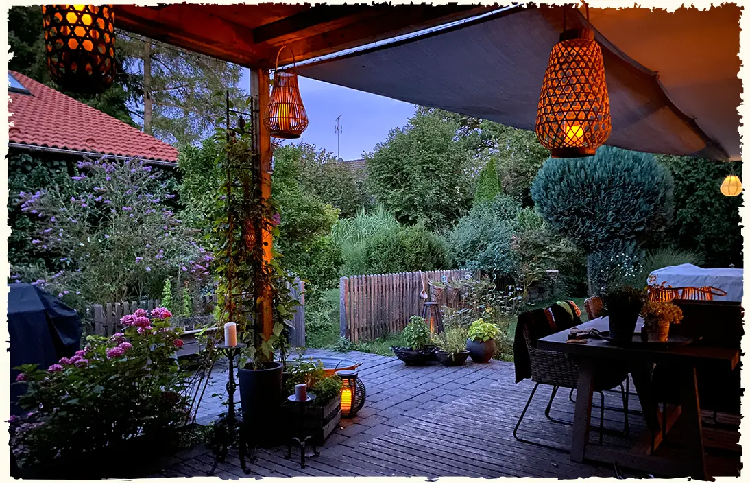 Abendstimmung auf einer zauberhaft dekorierten Holzterrasse mit Blick in den Traumgarten und hängenden Korblaternen
