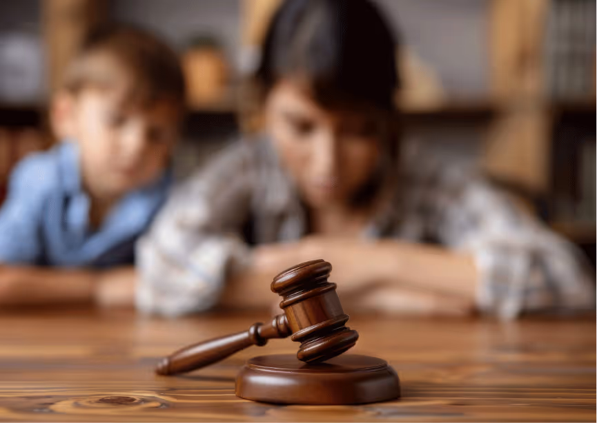 Un marteau de justice en bois au premier plan avec un enfant et une femme flous en arrière-plan semblant préoccupés.