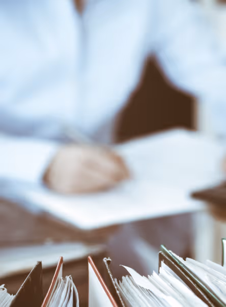 Dossiers de bureau alignés au premier plan avec une personne en chemise blanche écrivant en arrière-plan flou.