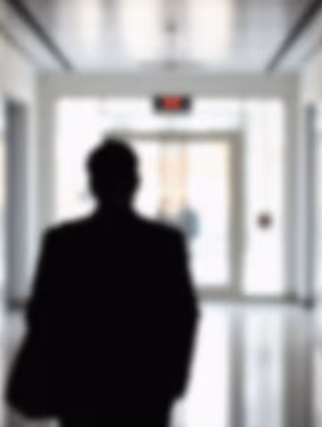 Silhouette floue d'une personne debout dans un couloir clair vers une sortie lumineuse.