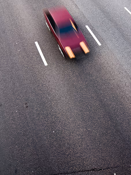 Voiture rouge floue roulant vite sur une route asphaltée avec des marquages blancs.