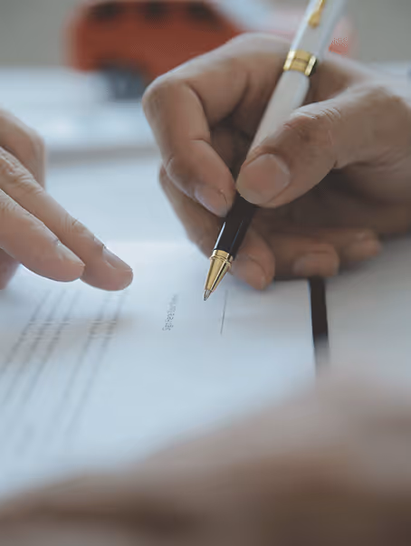 Une personne tenant un stylo, prête à signer un document sur une table.