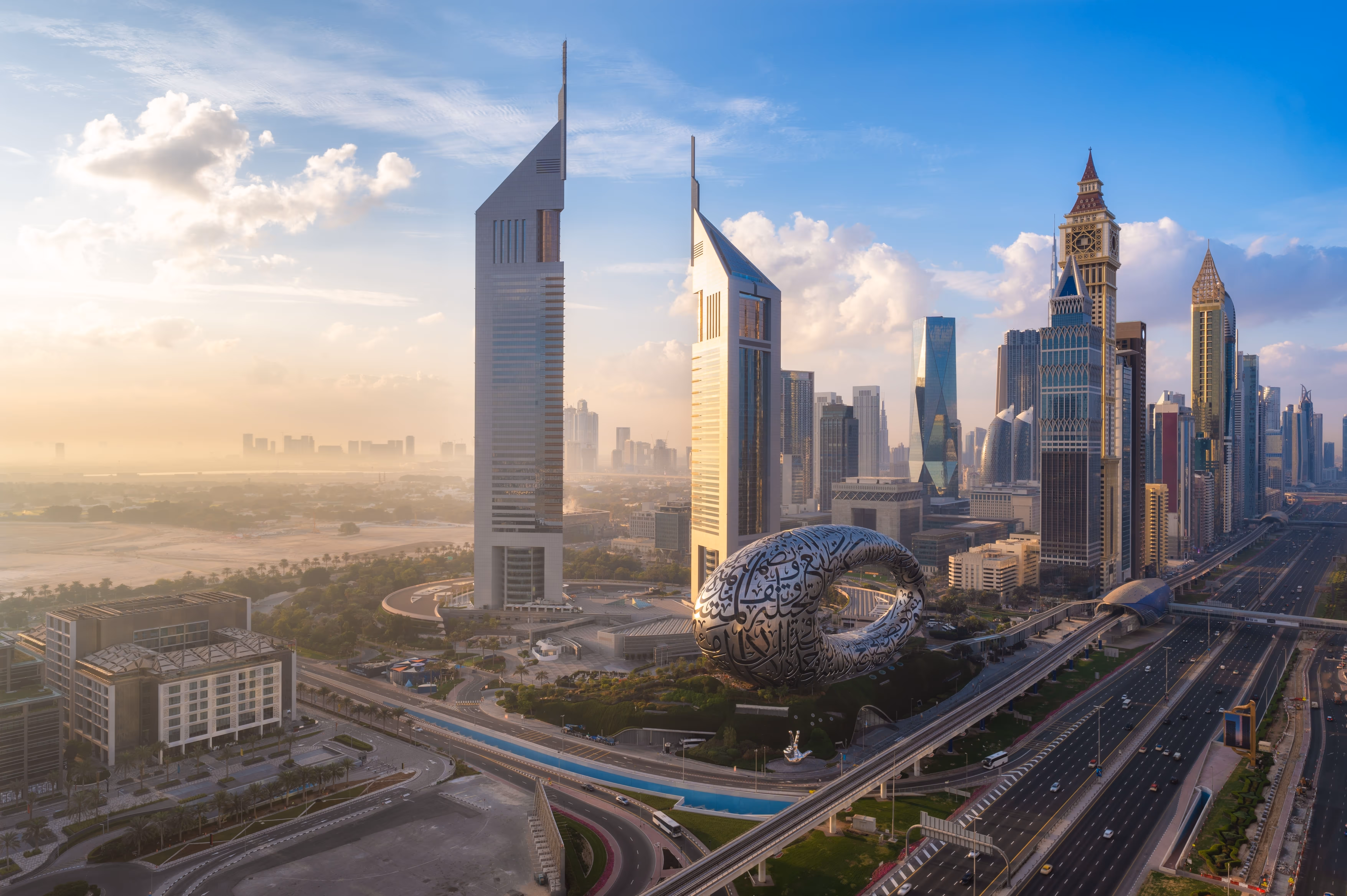 Dubai cityscape at sunrise featuring the Museum of the Future with Arabic calligraphy, Emirates Towers, and Sheikh Zayed Road.