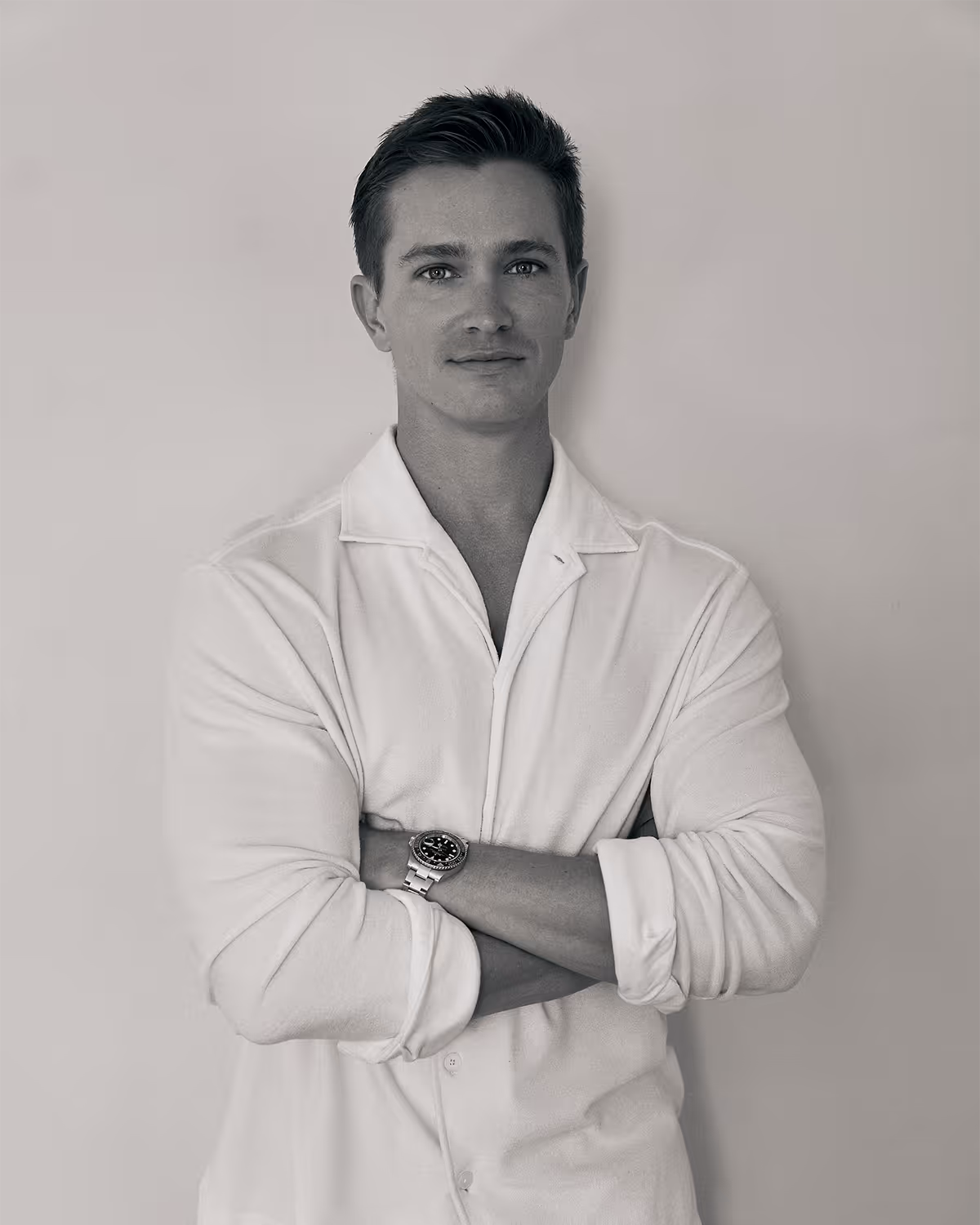 Kelan Berwick, co-founder of Scott Mitchell Workshop wearing a white shirt, arms crossed, standing against a plain wall.