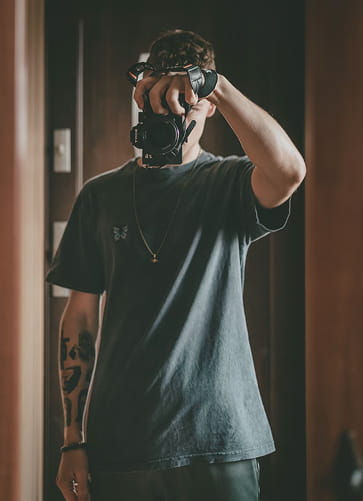 Person wearing a dark t-shirt taking a photo with a camera covering their face.