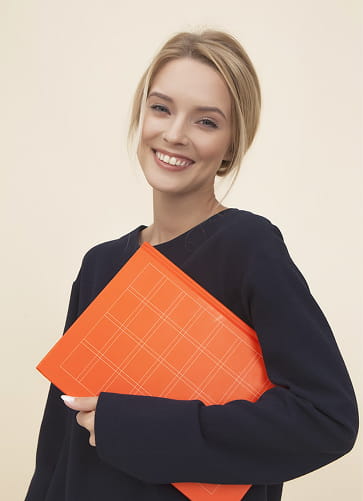 Smiling young woman with blonde hair holding an orange folder against a beige background.