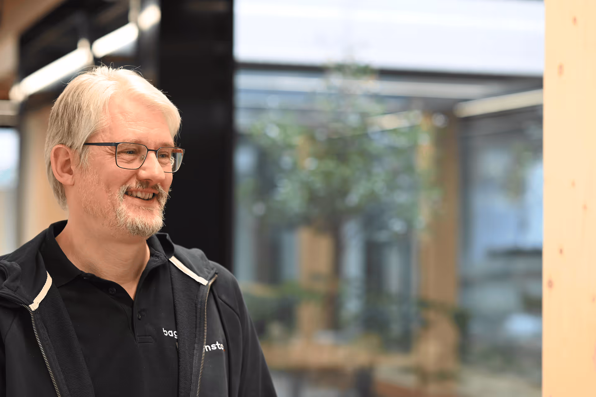 Portrait eines lächelnden Mitarbeiters mit Brille im Baggenstos-Polo im Foyer