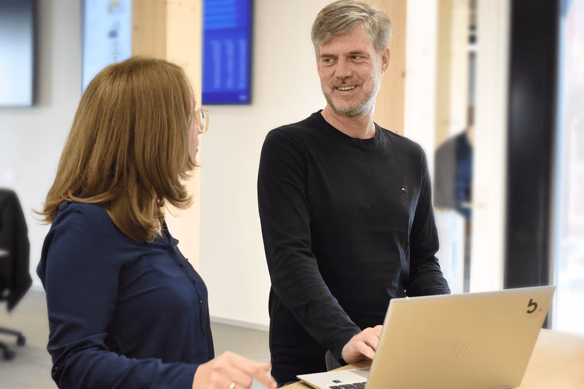 Mitarbeiterin und lächelnder Kollege im Gespräch über einen Laptop im modernen Büro