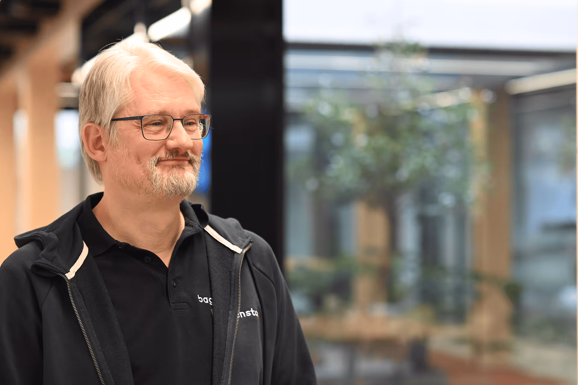 Portrait eines lächelnden Mitarbeiters mit Brille im Baggenstos-Polo im Foyer