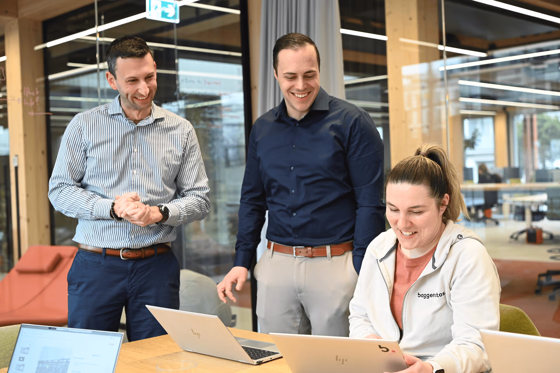 Drei lächelnde Mitarbeiter gemeinsam an einem Laptop im modernen Büro