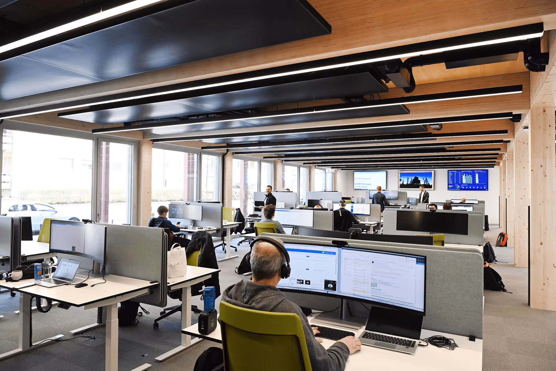 Modernes Grossraumbüro im Holzbau mit mehreren Arbeitsplätzen und Mitarbeitern an Bildschirmen