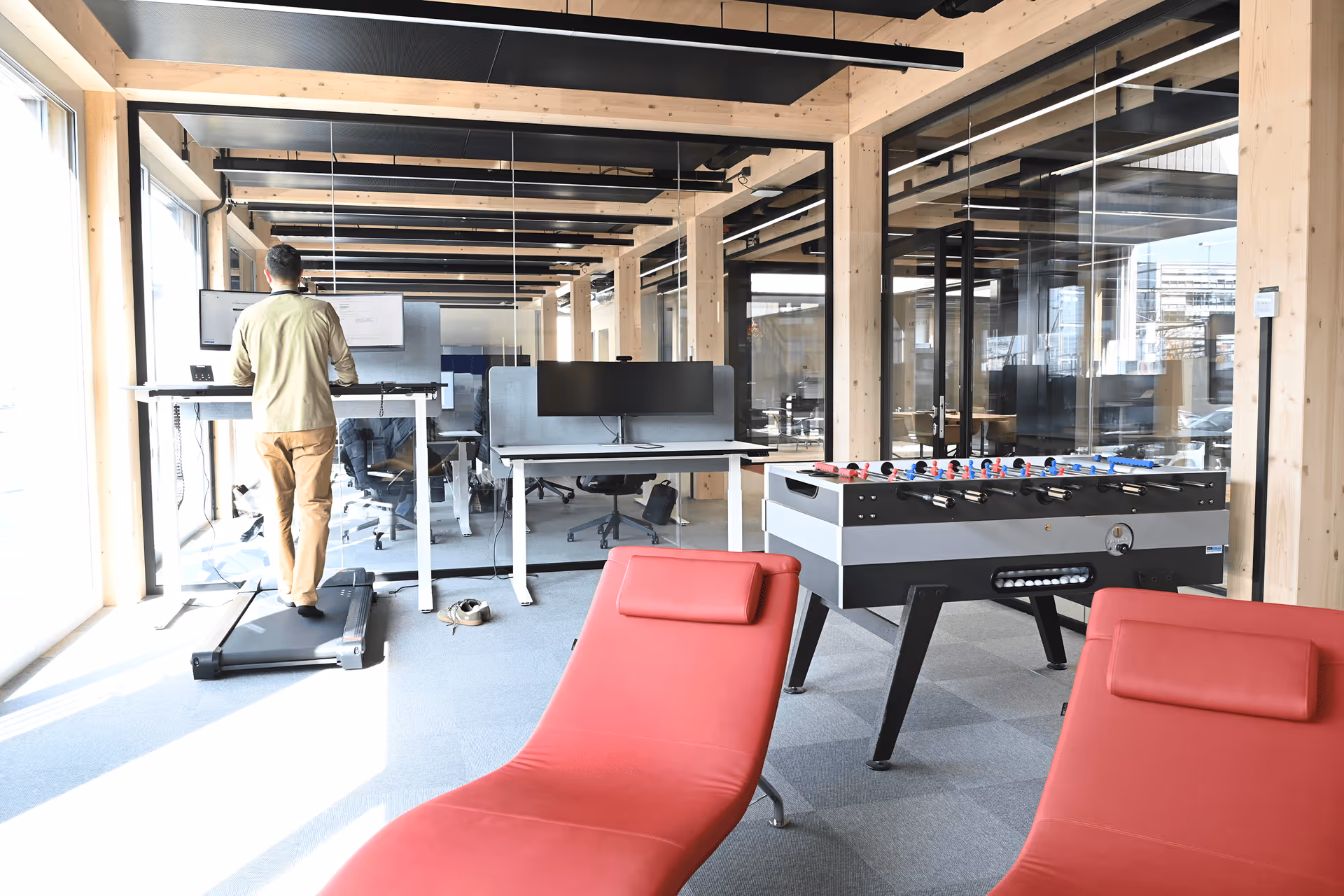 Moderner Holzbau-Arbeitsbereich mit Stehpult-Laufband, Tischfussball und roten Loungemöbeln