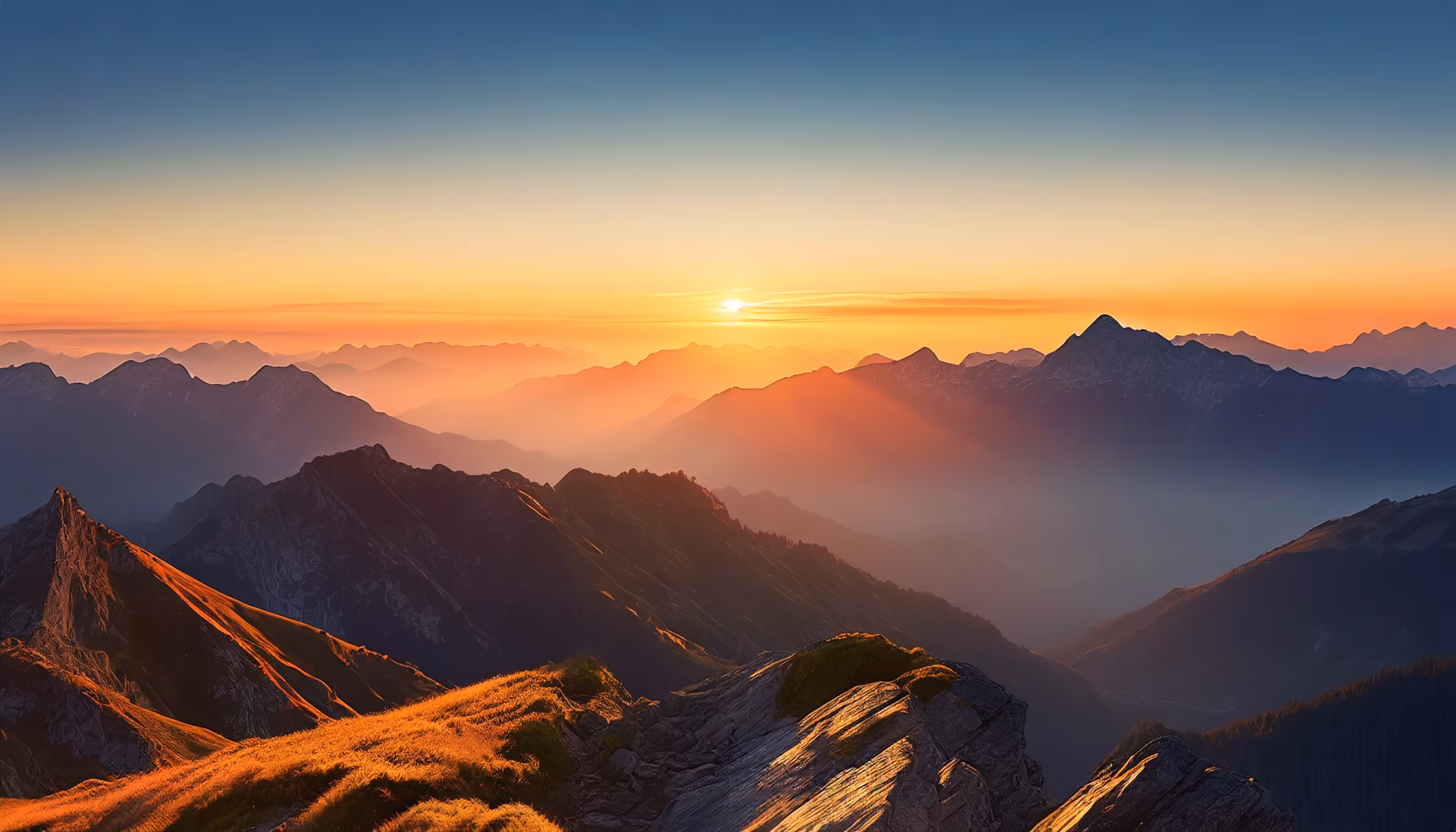 Bergpanorama bei Sonnenaufgang mit aufgehender Sonne über gestaffelten Gebirgskämmen und goldenem Gras im Vordergrund