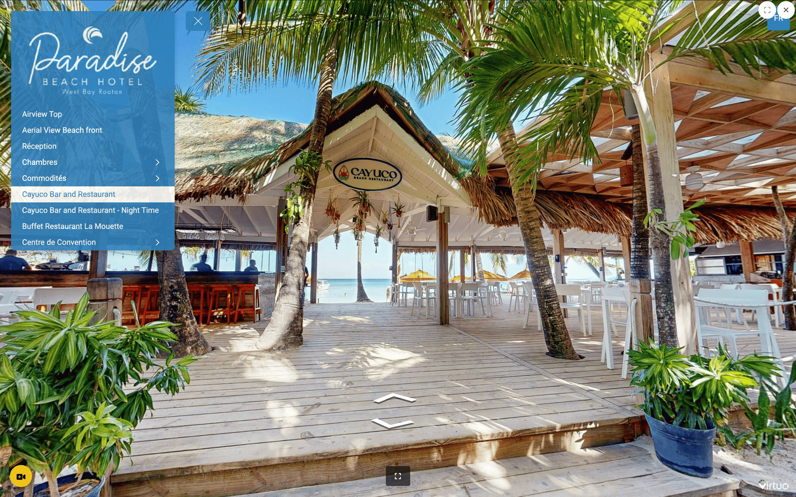 Open-air wooden deck with palm trees and tables under thatched roof at Cayuco Beach Restaurant overlooking the ocean.