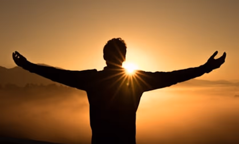 Silhouette of a person with arms outstretched against a golden sunrise or sunset.