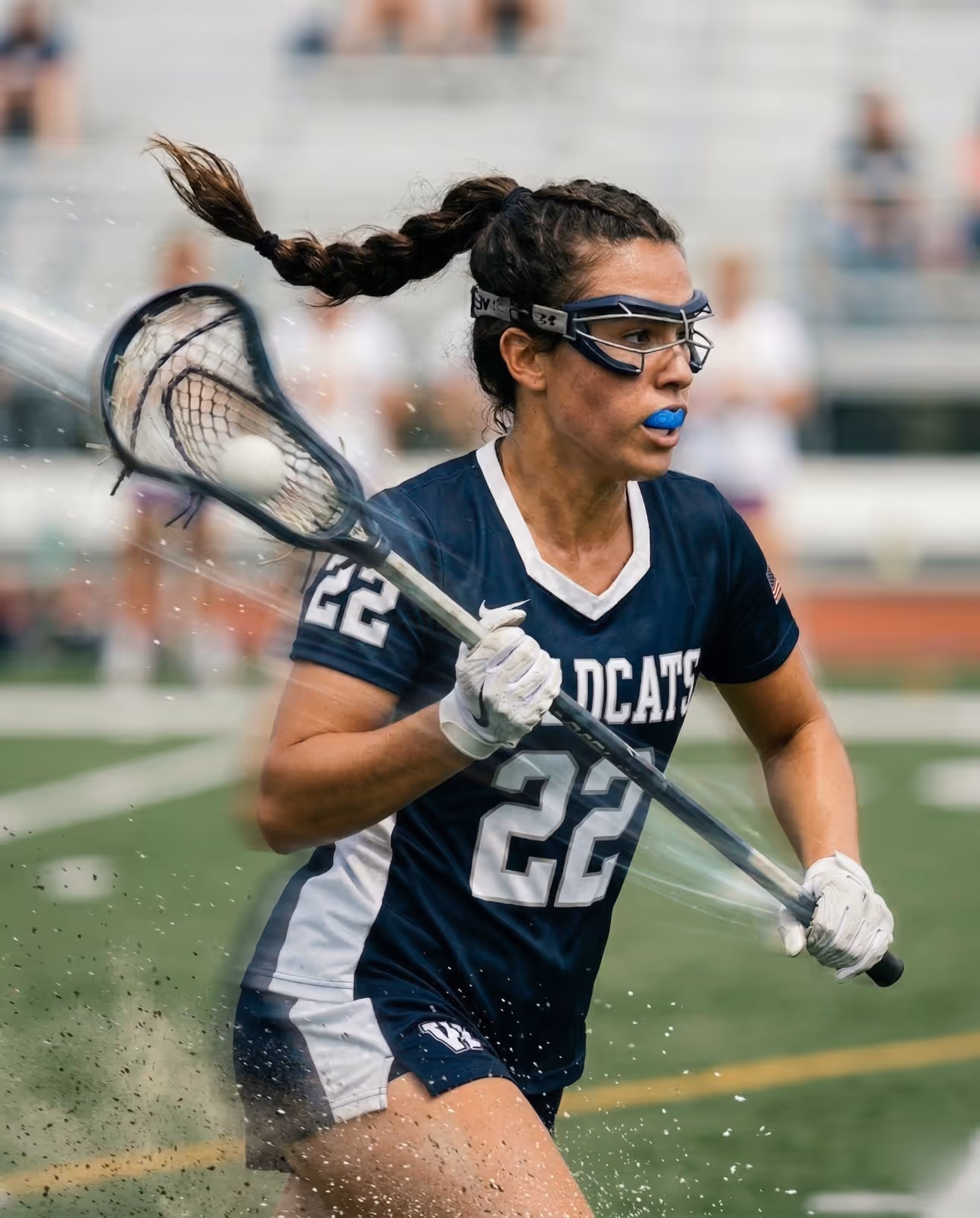 Female lacrosse player in black uniform running on turf field with a yellow ball in her stick.