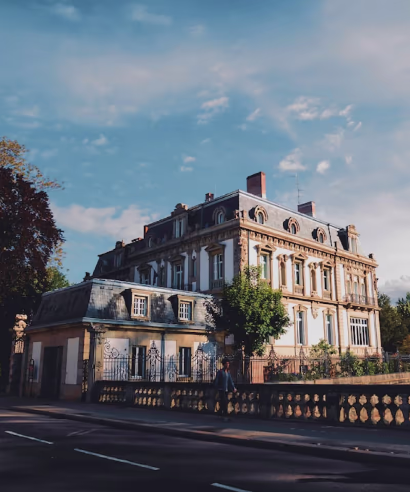 Bâtiment historique de style européen avec un toit mansardé sous un ciel bleu partiellement nuageux.