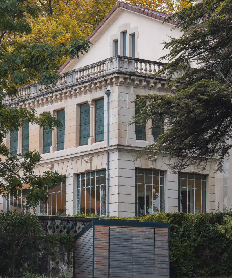 Façade d'une maison blanche de style classique avec fenêtres à vitraux, entourée d'arbres verts et jaunes en automne.