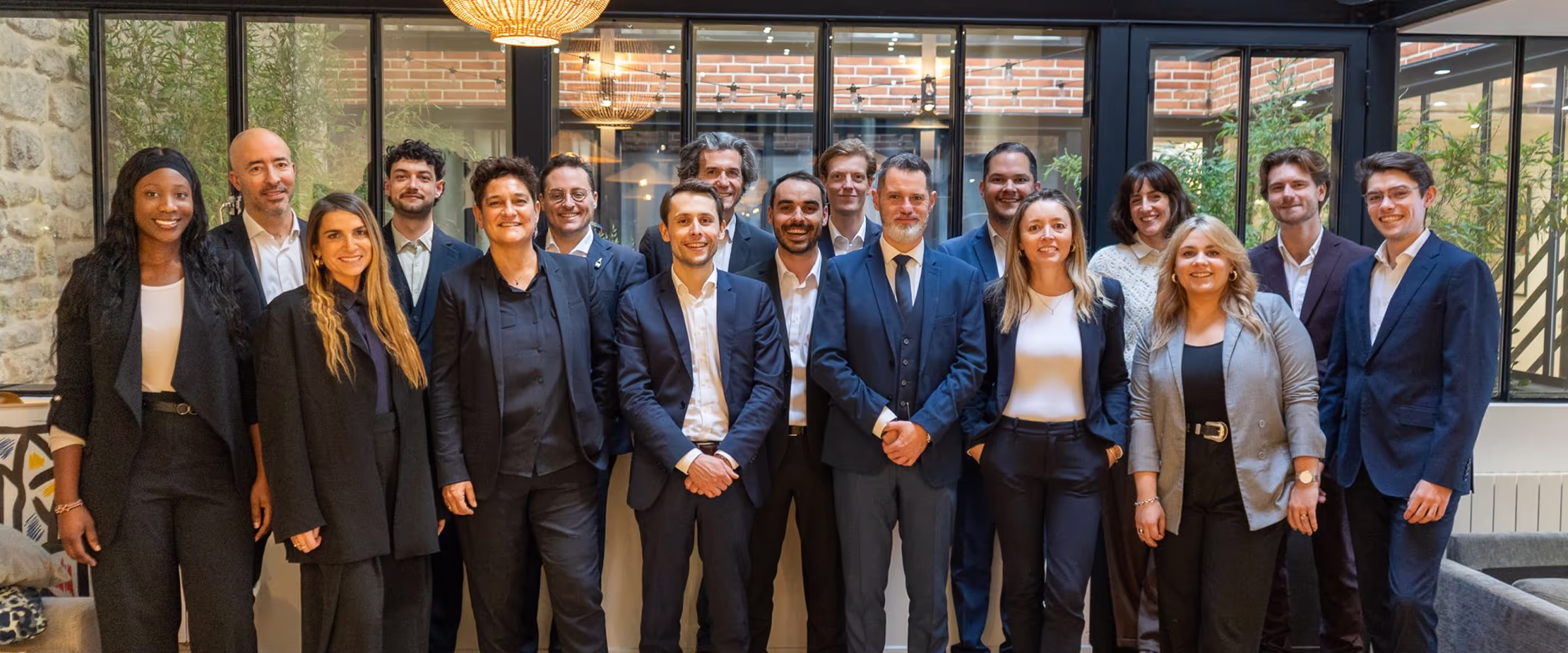 Groupe de 17 professionnels d'Osmose posant en tenue formelle dans un bureau moderne avec des fenêtres en verre et une décoration végétale.