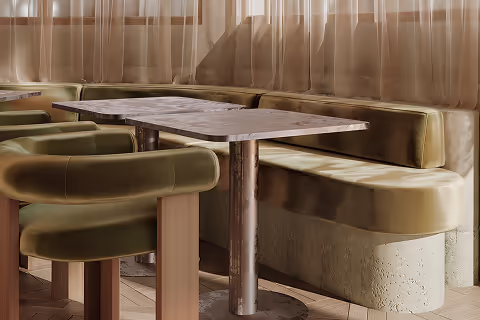 Coin repas avec une banquette et des chaises vertes autour d'une table rectangulaire en bois clair, éclairé par une lumière naturelle douce.