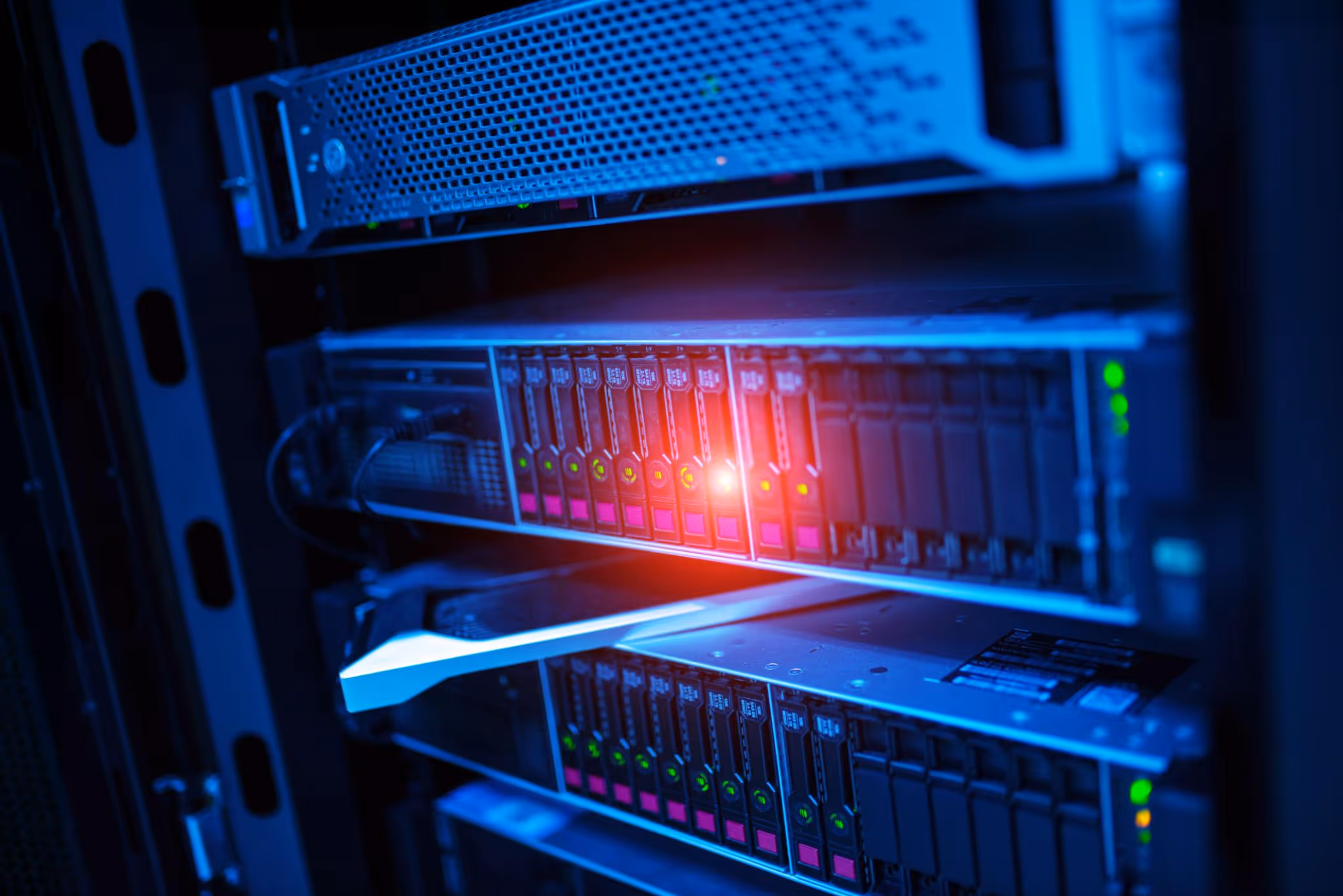 Close-up of server racks with blinking lights and one red warning light in a data center.