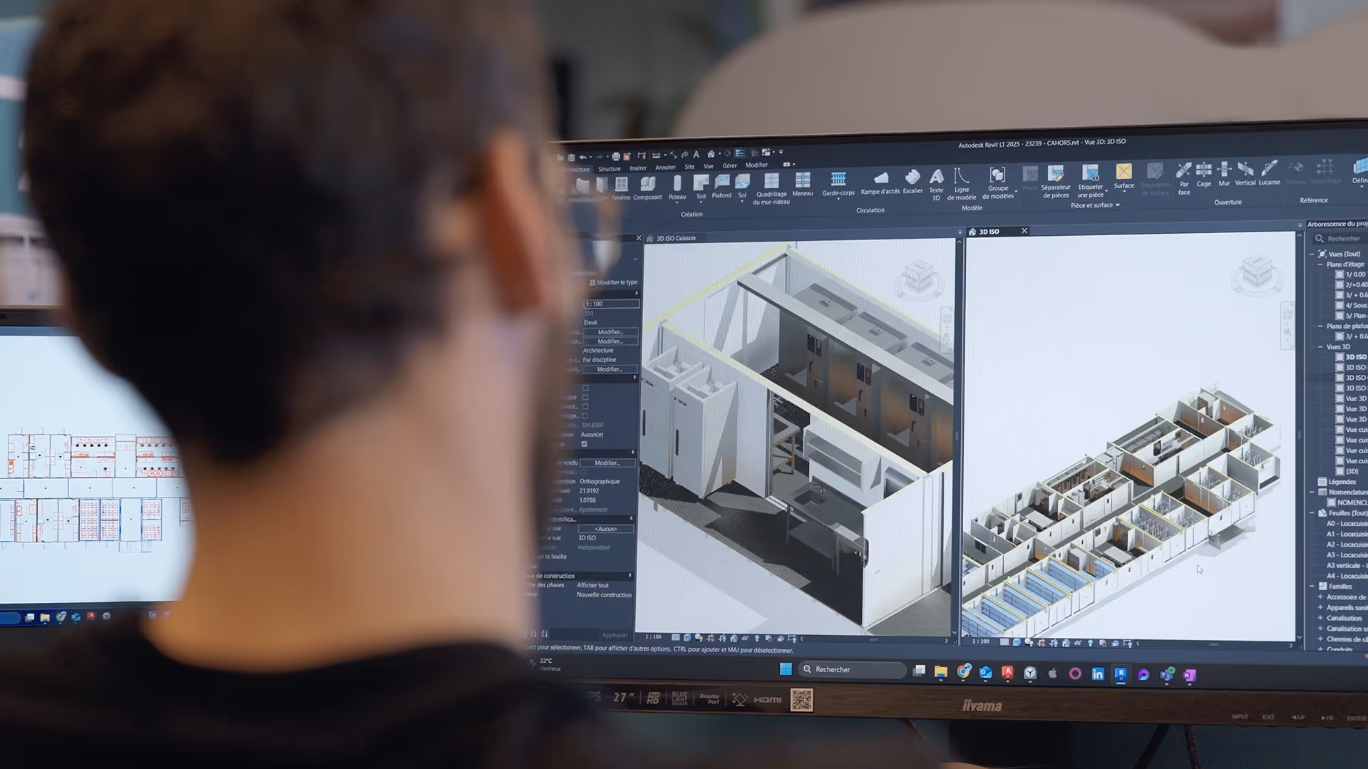 Vue arrière d'une personne regardant des plans architecturaux en 3D sur un écran d'ordinateur.