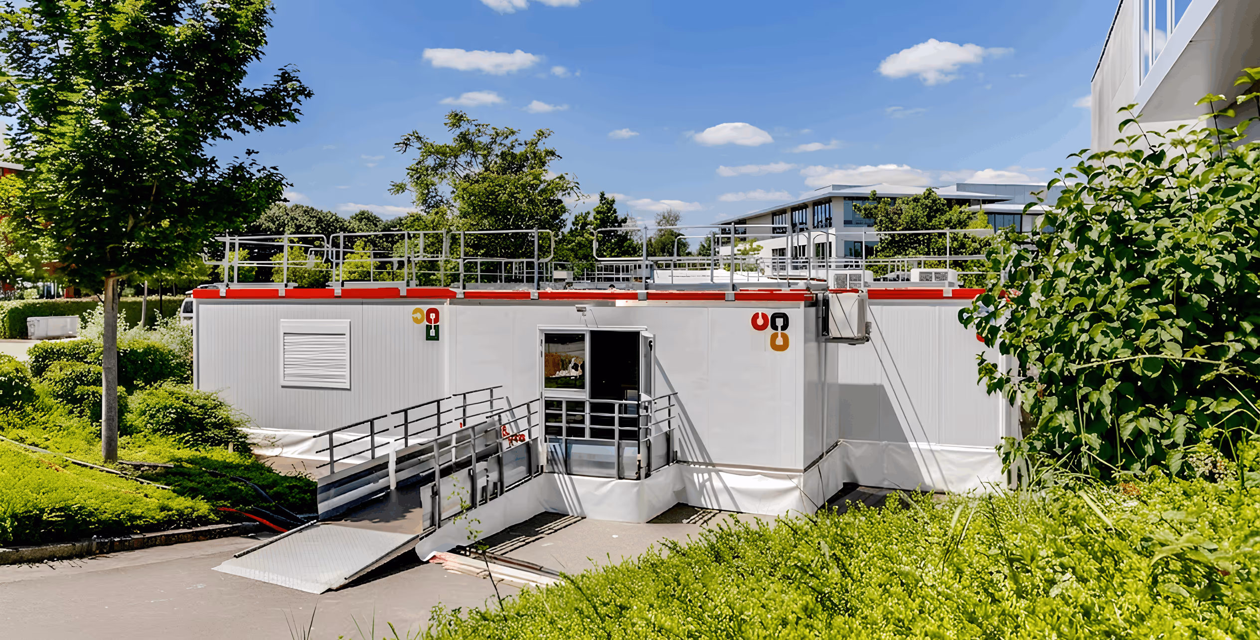 Cuisine modulaire professionnelle blanche avec rampe d'accès et arbres verts autour sous un ciel bleu.