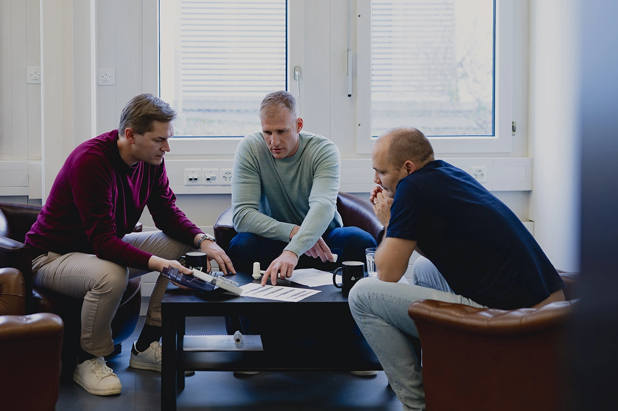 Die drei awalux Gründer in einer technischen Besprechung. Auf dem Tisch liegen merhrer technische Zeichnungen, Modelle von Zahnimplantaten und ein Chirurgie Tray.